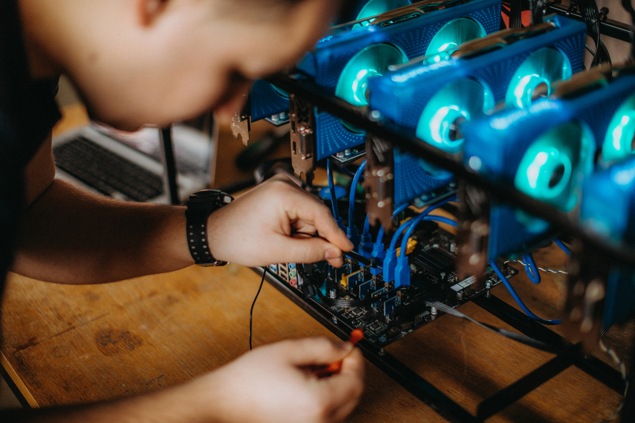 Close-up of hands assembling a computer motherboard inside an open PC case with blue LED cooling fans.