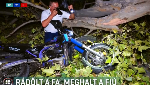 News photographer with flashlight filming a blue motorcycle crushed by a fallen tree at night (RTL logo in corner).