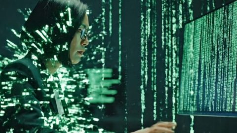 A woman in glasses working at a computer surrounded by cascading green code, symbolizing hacking or cybersecurity work.