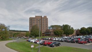 Brick mid-rise building with a large parking lot in front and trees along the perimeter. Clear sky above.