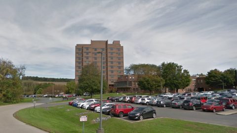 Brick mid-rise building with a large parking lot in front and trees along the perimeter. Clear sky above.