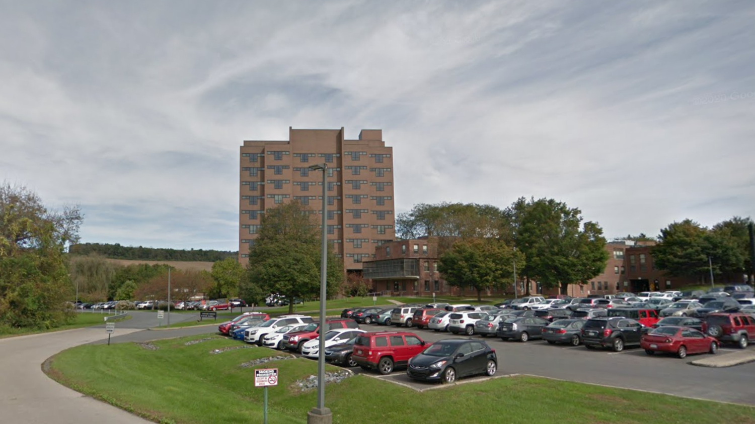 Brick mid-rise building with a large parking lot in front and trees along the perimeter. Clear sky above.