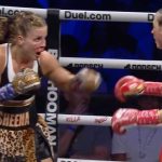 Left boxer wearing leopard print shorts labeled 'SHEENA' throws a punch toward her red-outfitted opponent in the ring.