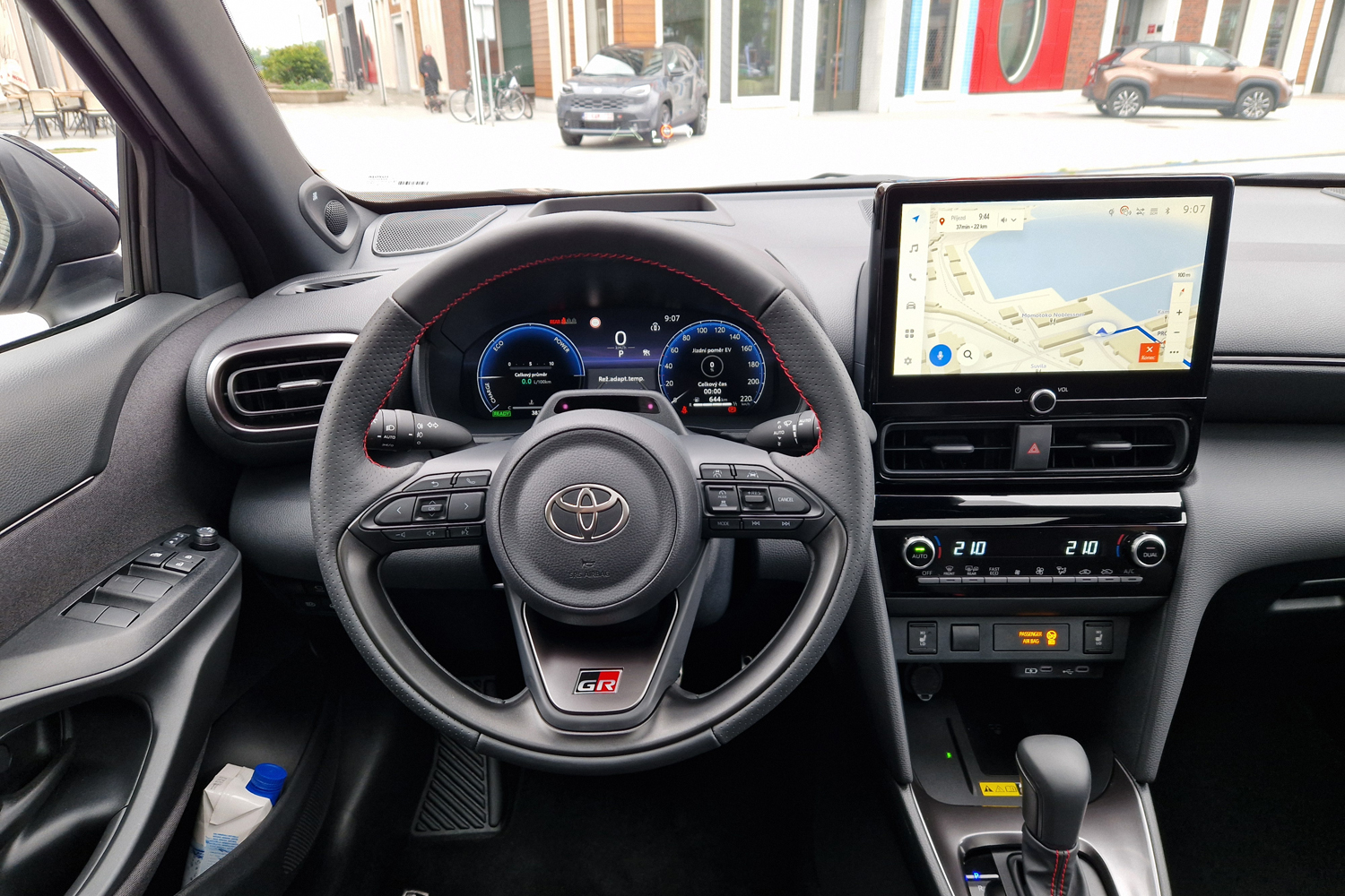 Car cockpit with steering wheel, digital instrument cluster, and a large touchscreen navigation.