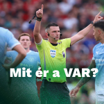 Soccer referee in a bright yellow shirt signals a VAR decision with both arms raised as players in blue surround him on the pitch. Crowd is blurred in the background, and a white Ziccer logo is in the corner.