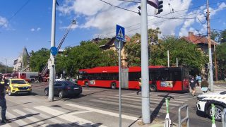 Red city bus stopped at a crosswalk with pedestrians nearby on a busy street.