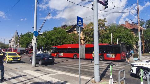 Red city bus stopped at a crosswalk with pedestrians nearby on a busy street.