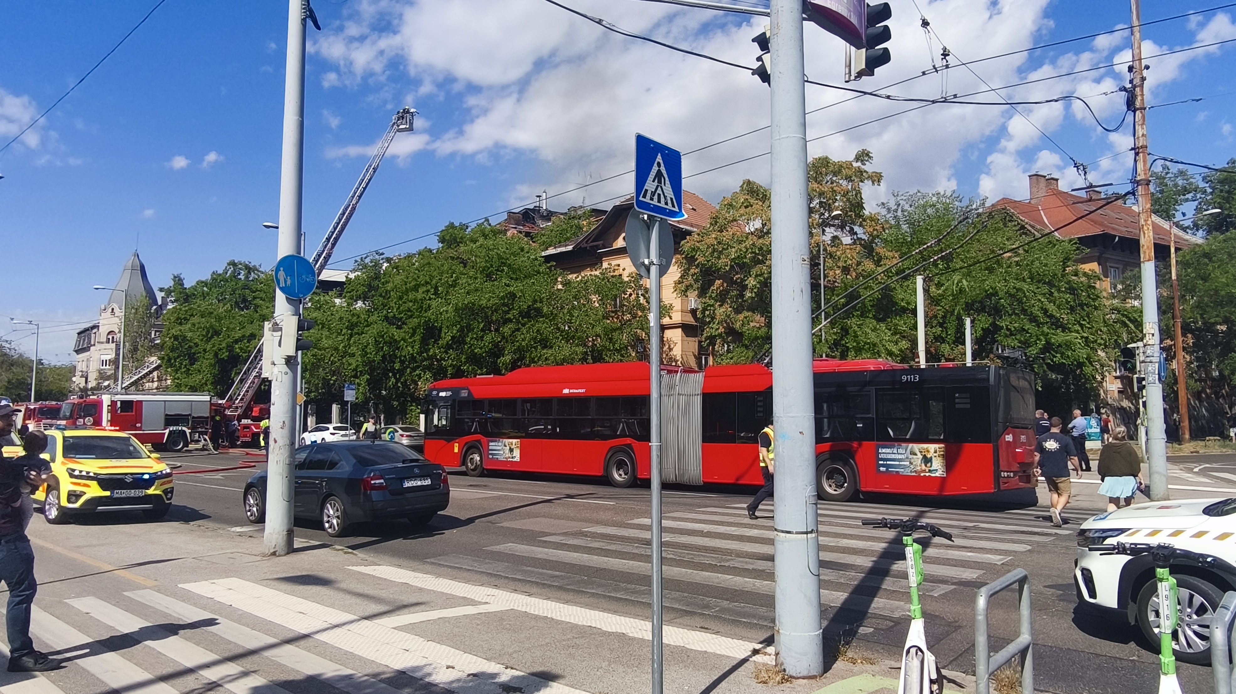 Red city bus stopped at a crosswalk with pedestrians nearby on a busy street.
