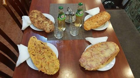 Overhead view of a wooden table with four plates of large fried breaded cutlets around a center arrangement of salt shakers and glass bottles, in a casual dining setting.