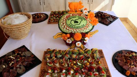 Table laden with meat canapés and a decorative watermelon centerpiece carved into a circle with flowers and a small orange pig figure on top.