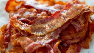 Close-up of crispy fried bacon strips with rendered fat and crisp, golden edges on pink meat.