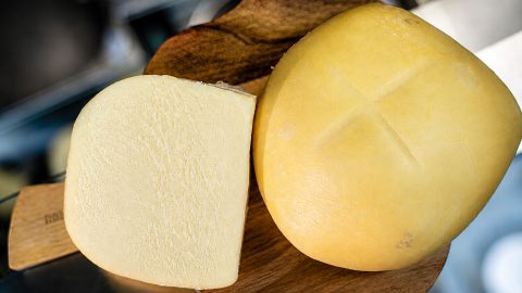Round wheels of yellow cheese on a wooden board with a sliced block showing pale interior.