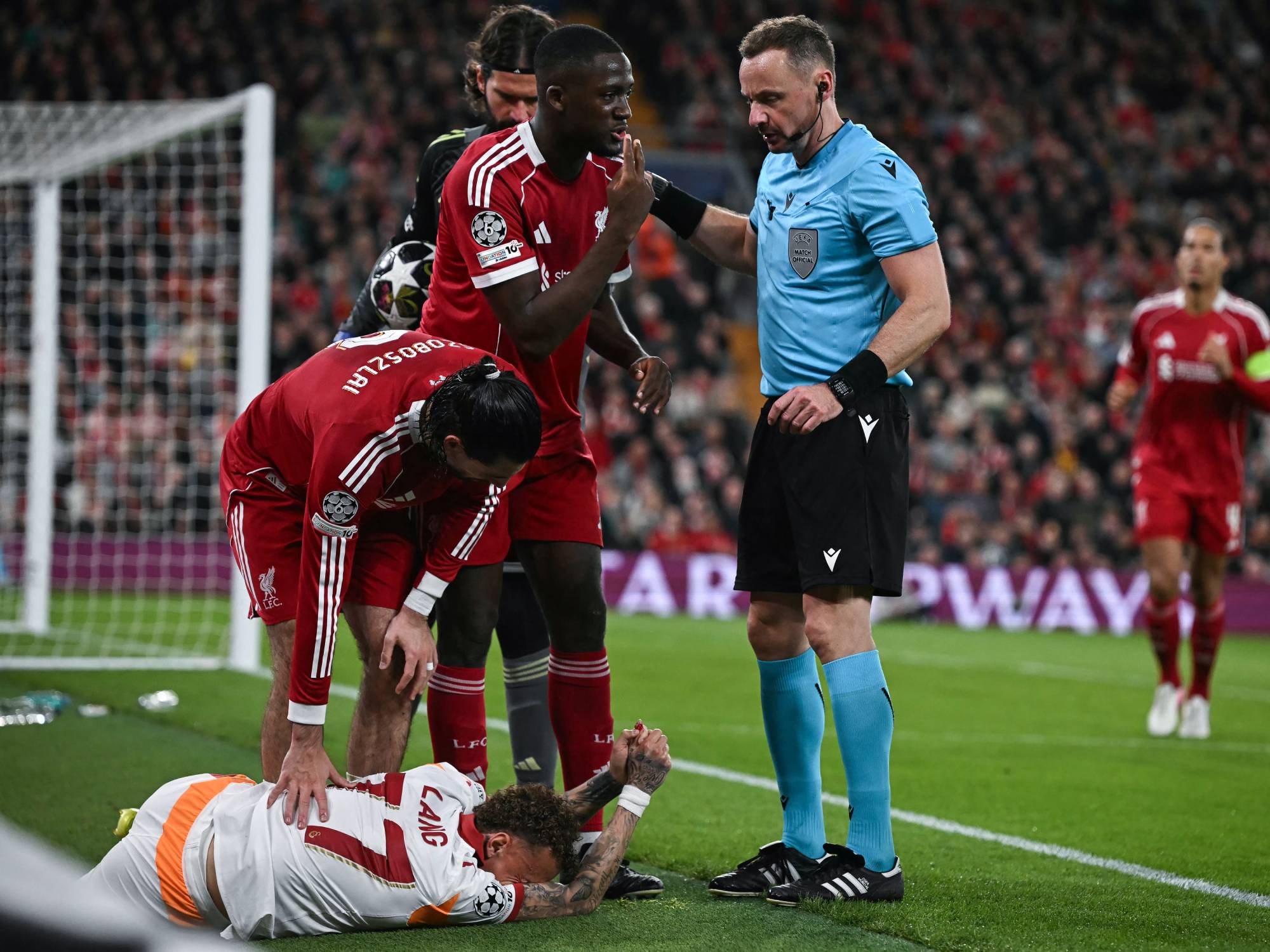 Galatasaray's Dutch forward #77 Noa Lang (DOWN) reacts on the floor next to Polish referee Pawel Raczkowski (R), Liverpool's Hungarian midfielder #08 Dominik Szoboszlai (C) and Liverpool's French defender #05 Ibrahima Konate after cutting his thumb during the UEFA Champions League, round of 16 second leg football match between Liverpool and Galatasaray at Anfield in Liverpool, north-west England on March 18, 2026.